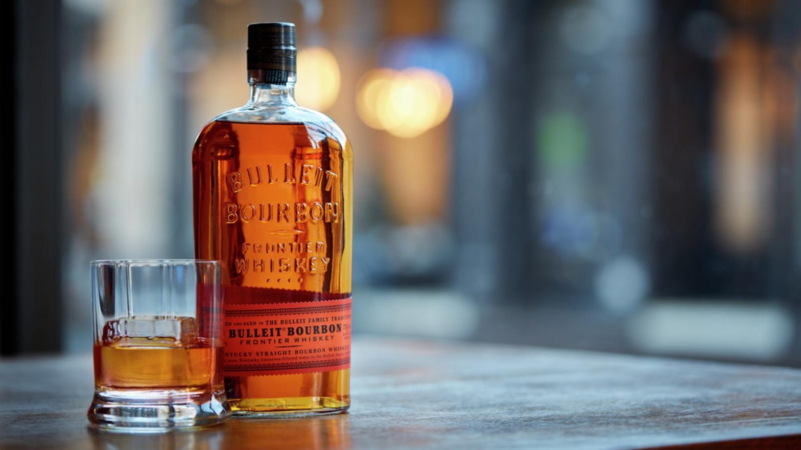 Imagem mostra garrafa de whiskey Bulleit Bourbon ao lado de copo baixo com whiskey.